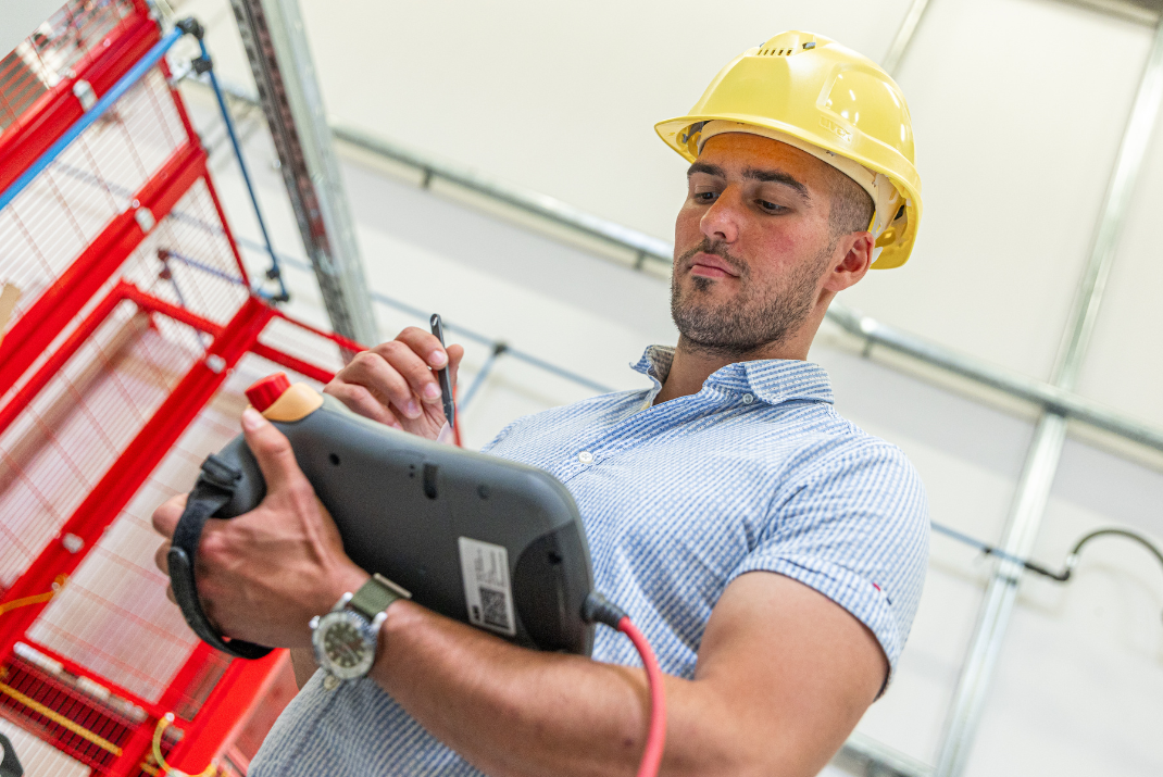 Berti from Diatron noting something into a monitor in his hands while wearing a yellow safety helmet in the production hall