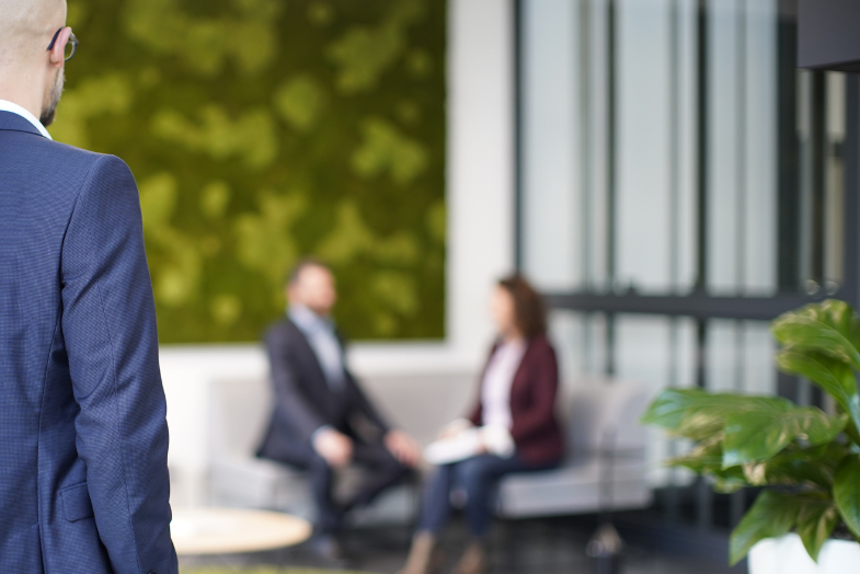 STRATEC employee looking at two other colleagues sitting on the sofa in the reception area STRATEC employee looking at two other colleagues sitting on the sofa in the reception area