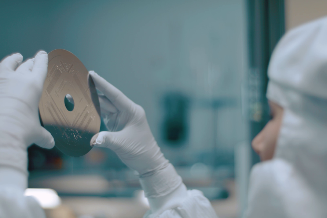 A laboratorian with safety gloves and head cover holding up a medical disc with engravings 