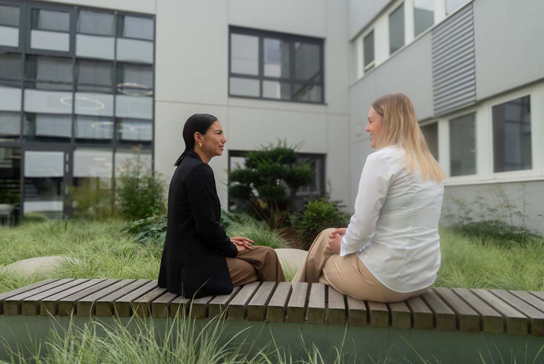 Two female STRATEC employees talking with each other on the bench outside of the headquarters in Birkenfeld, Germany