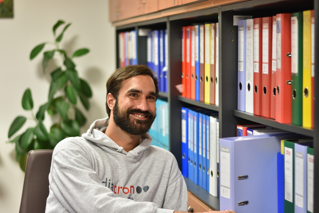 A Diatron employee smiling with several folders and a plant in the background
