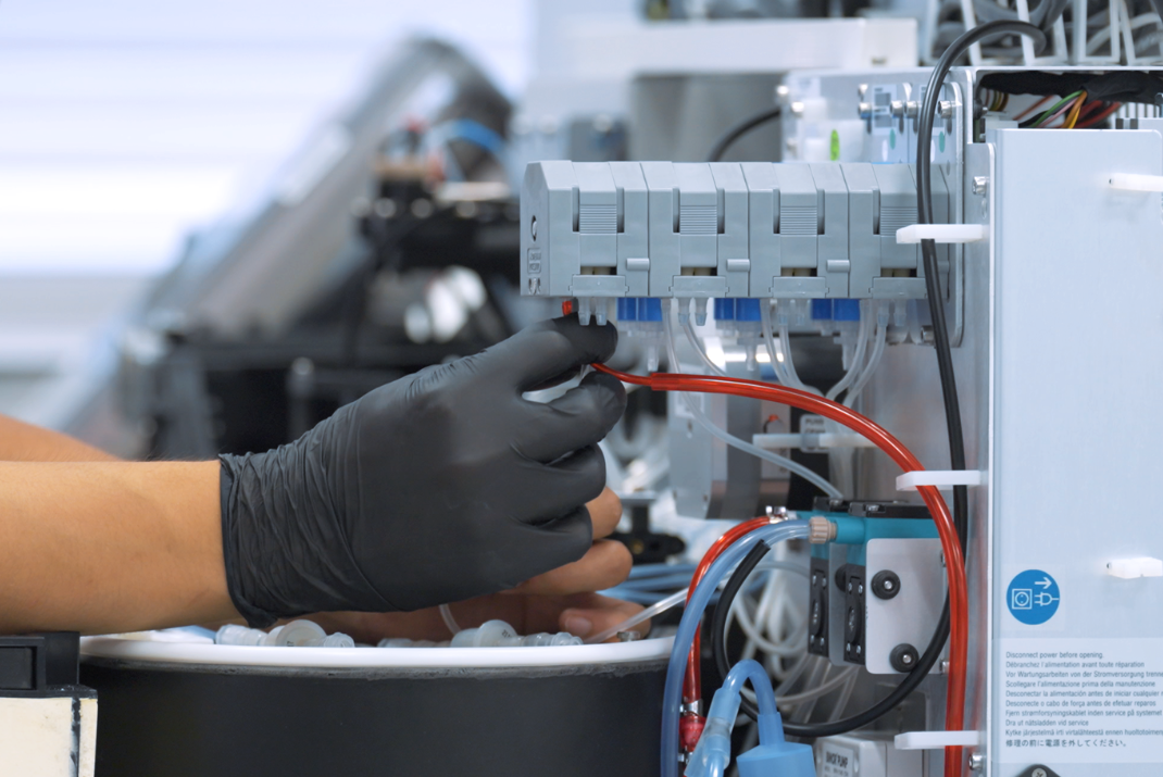 Laboratorian with black safety gloves pulling out a cable from the laboratory machine