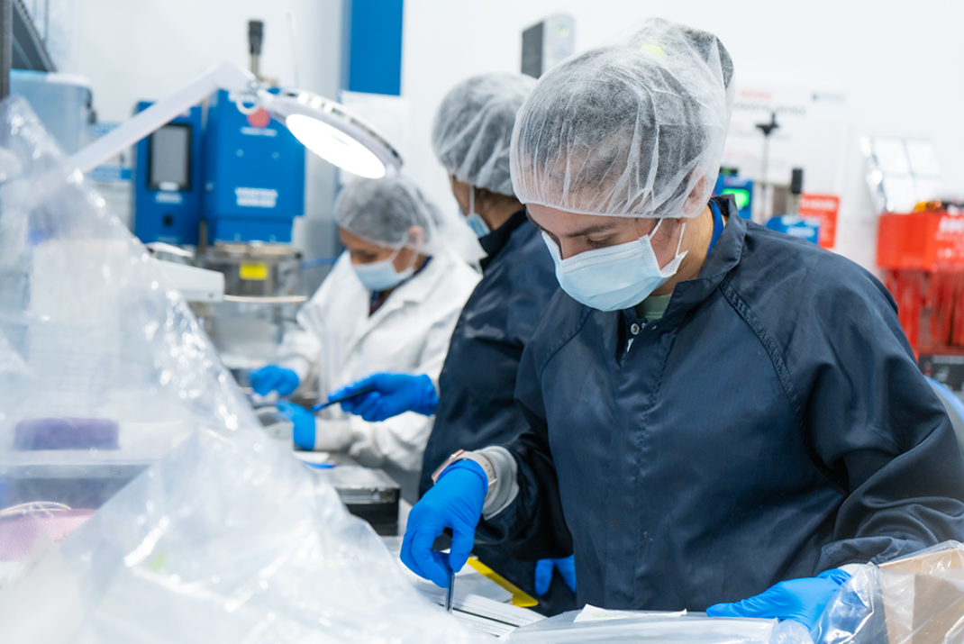 Natech employees with protective hoods, masks and gloves preparing the testing tubes in the production hall