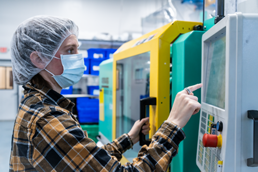 Natech colleague wearing a protective hood and mask operates a machine in the production hall