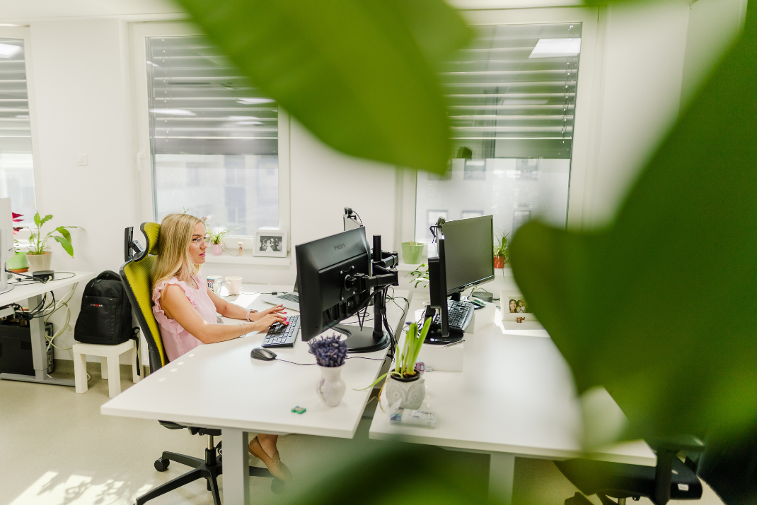 STRATEC employee working in the office with leaves of a plant in the foreground 